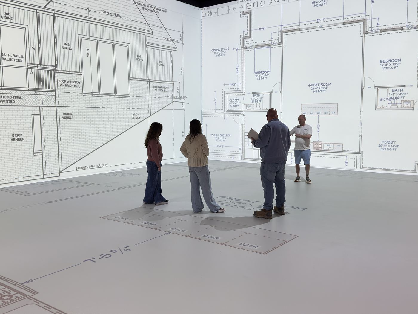 A family reviewing their home's floor plans and elevations projected across the walls and floor of a pADS design room