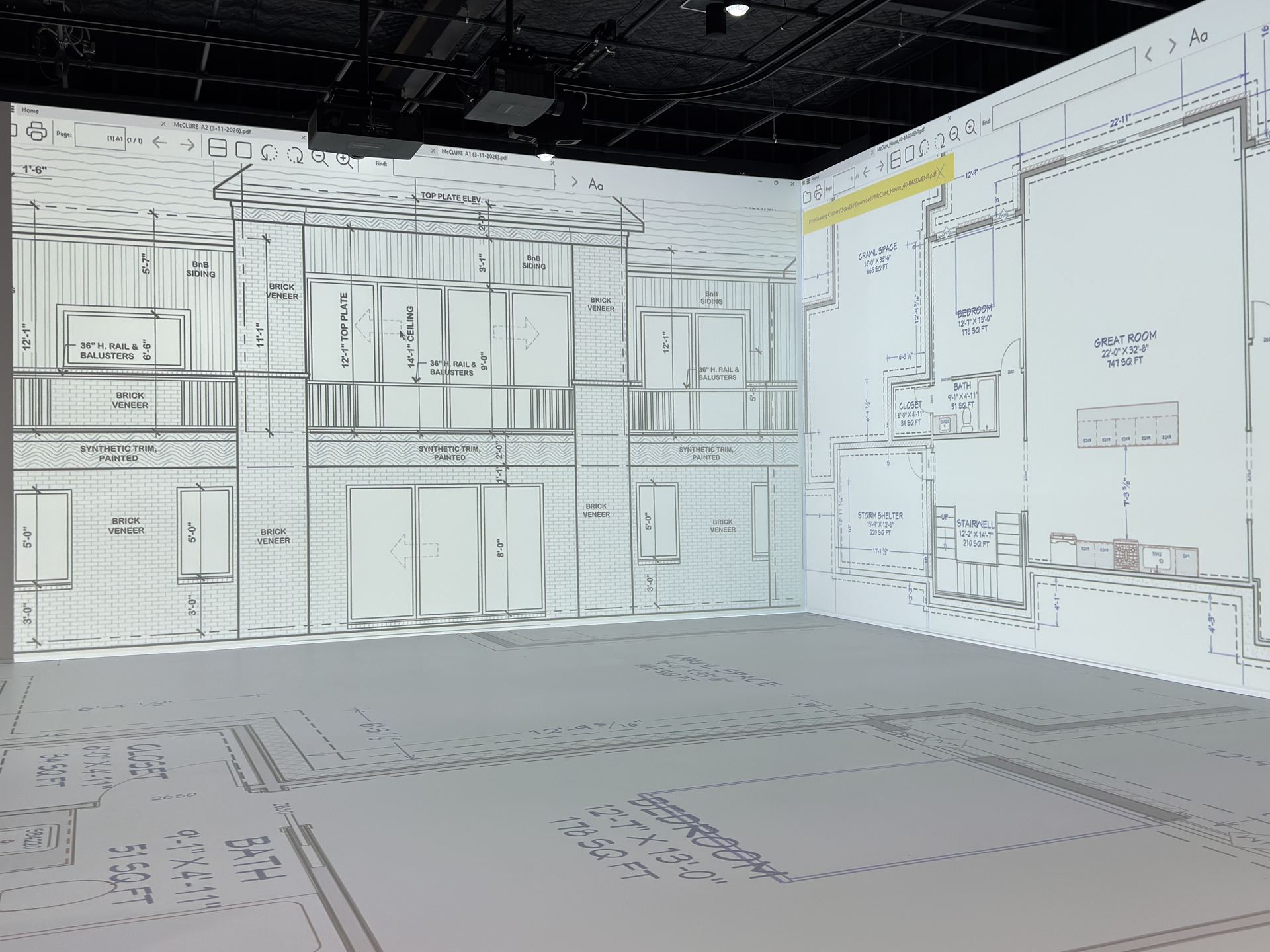 Architectural elevations and floor plans projected at full scale across the walls and floor of a pADS design room